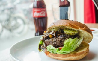 um hambúrguer com salada e carne num prato e uma refrigerante ao lado